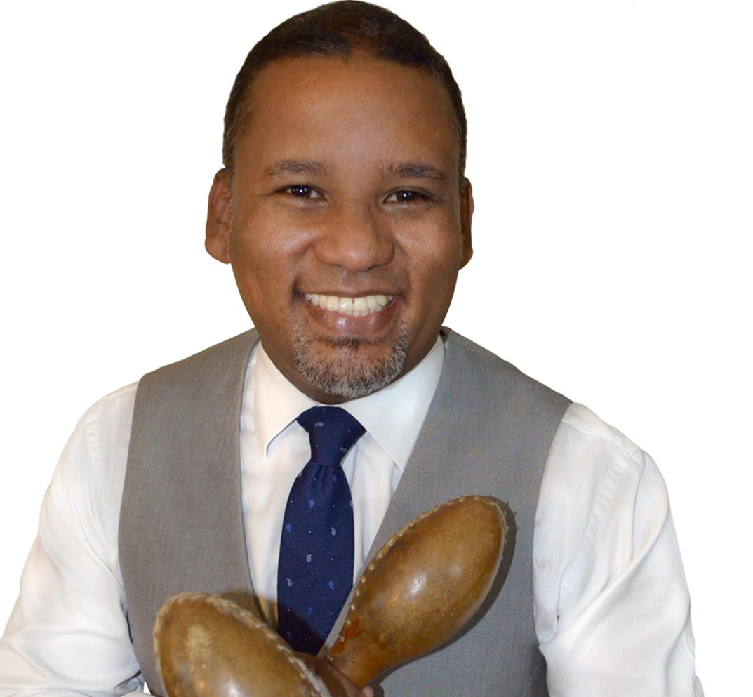 CARLOS Smiling man holding maracas, wearing a tie.